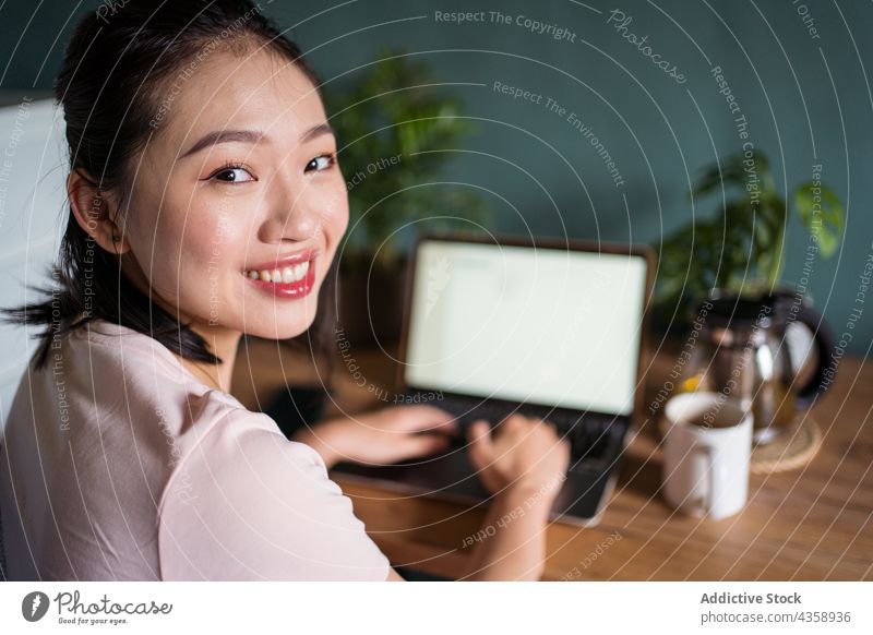 Delighted Asian woman reading document on laptop and working at home freelance smile computer female asian delight ethnic netbook job happy cup online using