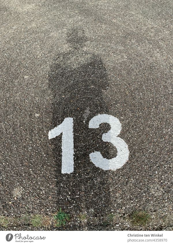 The number 13 in white paint on rough grey asphalt and the shadow of the photographer I drawn & painted thirteen Asphalt Shadow Street Parking lot