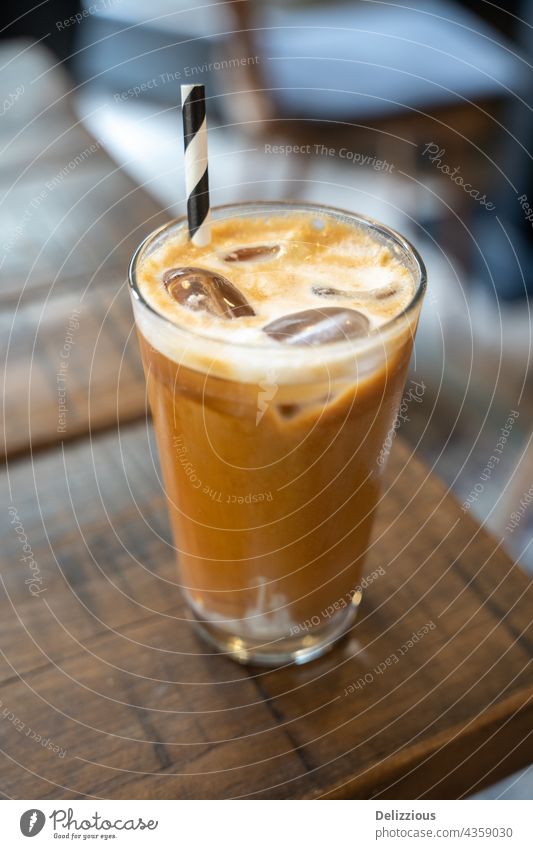 Side view of a ice latte coffee with a straw on a wooden table coffee latte milk cold drink ice cube ice cubes cafe cafeteria caffeine closeup background glass