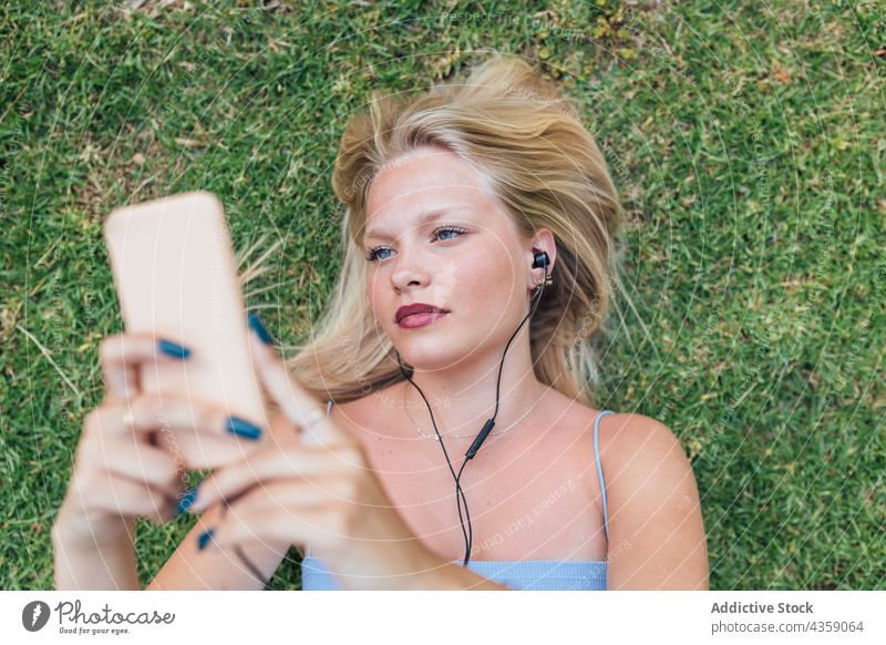 Carefree woman listening to music on lawn dreamy earphones lying grass song female enjoy park relax harmony summer rest audio sound serene weekend meadow