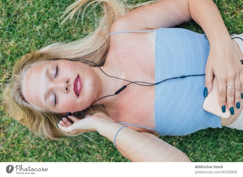 Carefree woman listening to music with closed eyes on lawn carefree dreamy eyes closed earphones lying grass song female enjoy park relax harmony summer rest