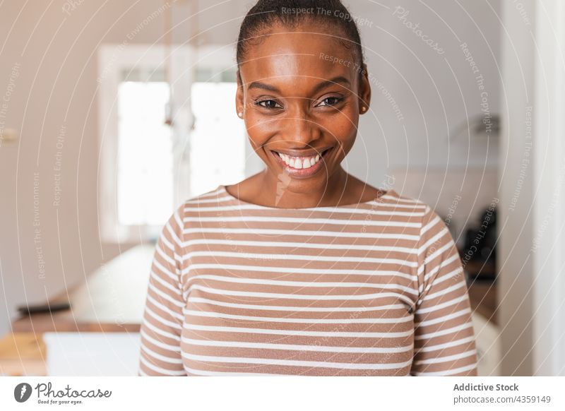 Black woman in wear with striped ornament at home confident gaze window appliance kitchen portrait table stare washing machine kettle electric hang light bulb