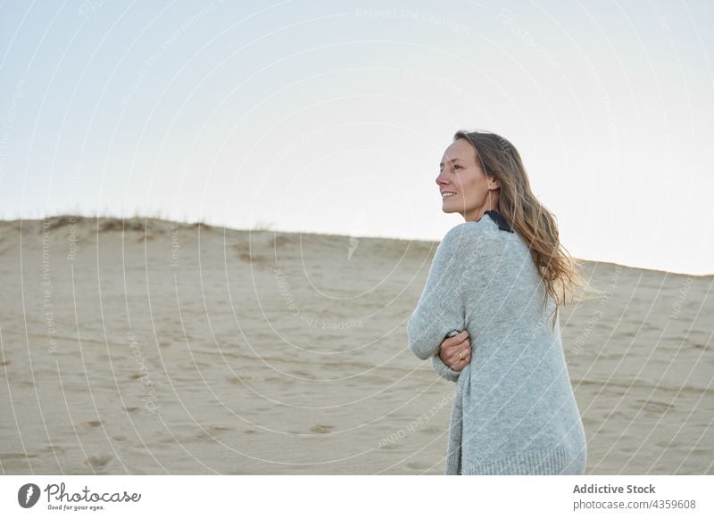 Smiling woman standing on sandy seashore in summer beach enjoy sunset evening smile vacation female coast seaside water content carefree ocean travel cheerful
