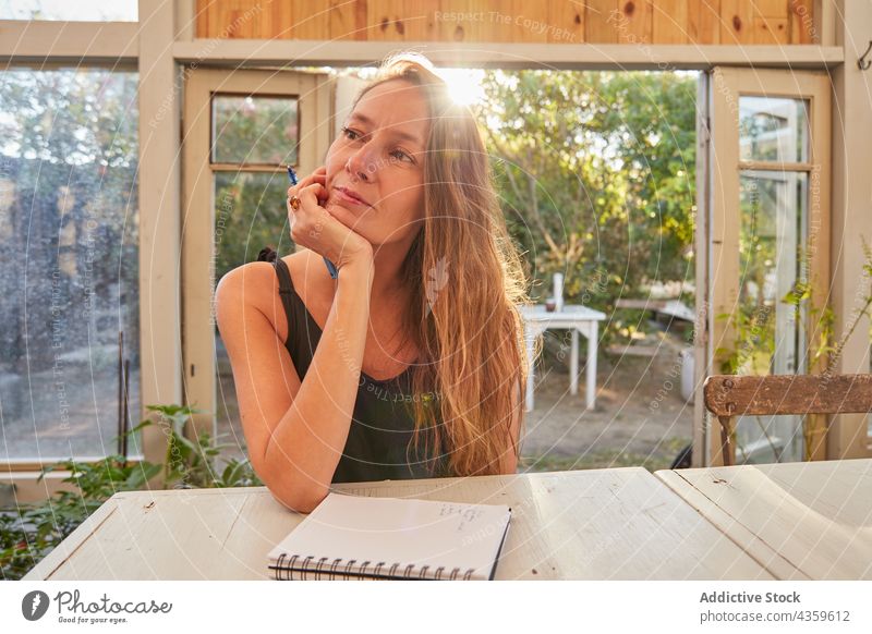 Smiling woman taking notes in notebook in glasshouse write notepad greenhouse gardener smile cheerful work female plant occupation potted flowerpot pen botany