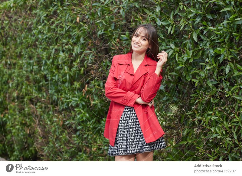 Smiling young woman in red jacket standing in park style fashion trendy spring smile outfit outerwear female color happy cheerful apparel brunette modern