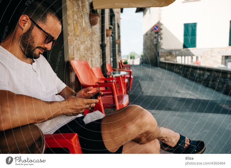 Man sits in an Italian street cafe on vacation and looks at his mobile phone Café Italy Summer Cellphone Sidewalk café Tourist Old town Tourism