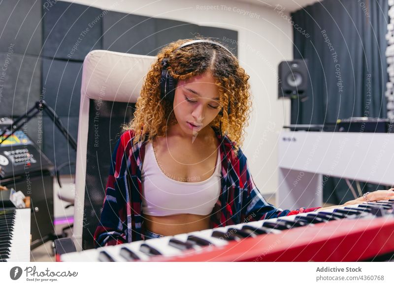 Black vocalist playing synthesizer while singing into microphone in studio song headset woman using gadget device singer music headphones instrument musical