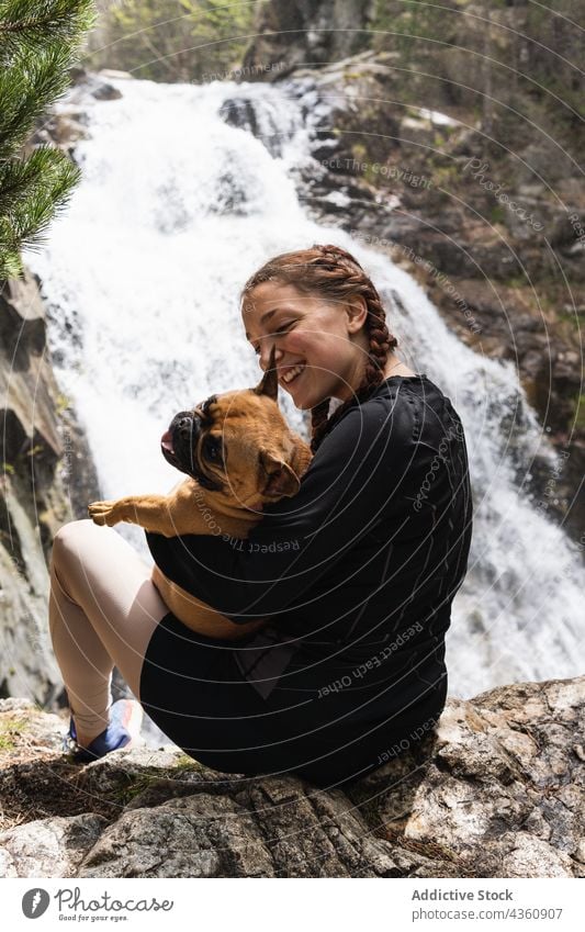 Cheerful traveling woman with dog near waterfall in forest traveler animal hiker together pyrenees female french bulldog companion happy mountain highland