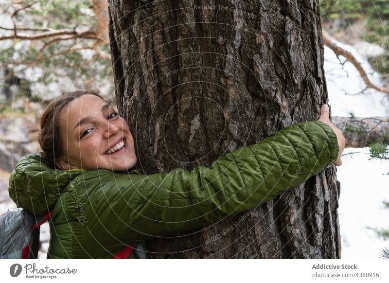 Smiling traveling woman hugging tree in woods forest traveler embrace trunk enjoy smile female pyrenees cheerful happy nature holiday positive outerwear