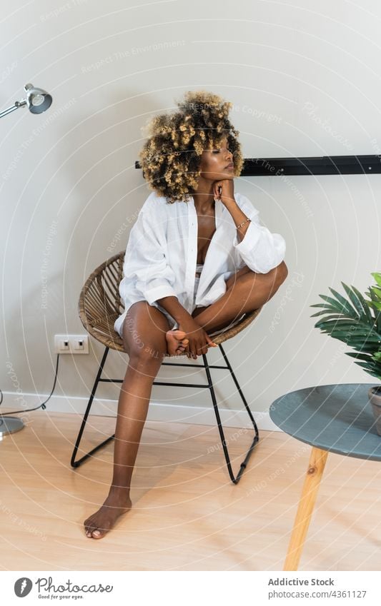 Black woman sitting in round chair in light room think tranquil concern ponder apartment lean on hand melancholy at home eyes closed dreamy female thoughtful
