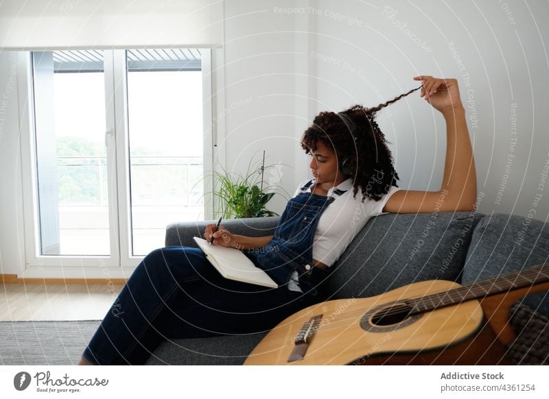 Black musician composing music at home woman compose thoughtful listen headphones notebook pensive creative notepad female ethnic black african american guitar