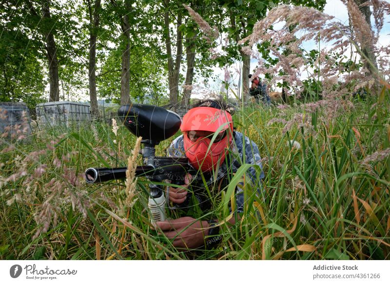Anonymous paintball player aiming at enemies hiding in grass men game team gun opposite entertain male opponent together target hide active shooter meadow field