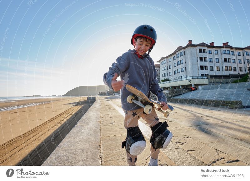 Smiling teen skater standing with skateboard on embankment boy seashore summer smile teenage activity enjoy cheerful happy sit promenade walkway carefree sport