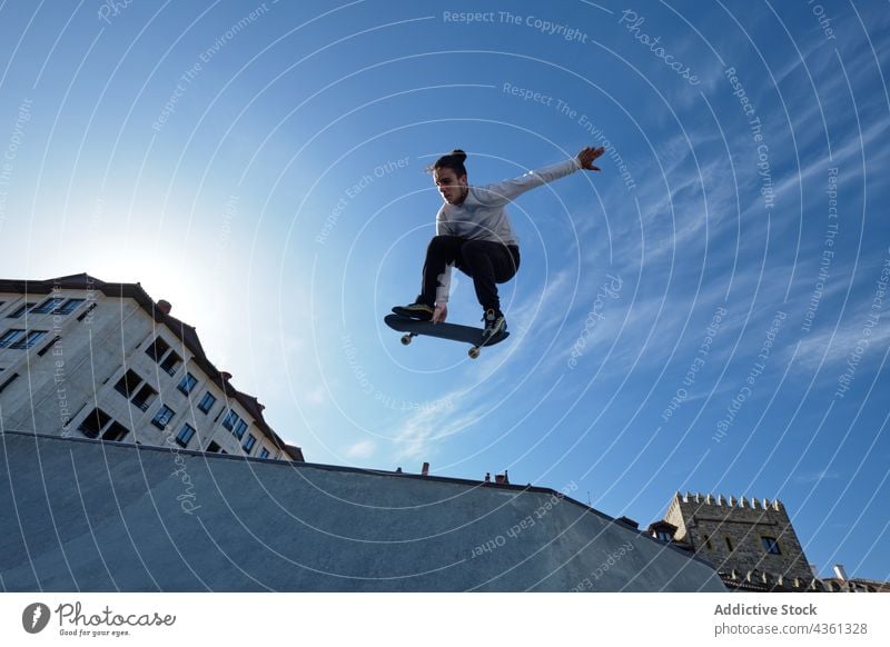 Man jumping with skateboard and showing trick in skate park skater man stunt ramp extreme adrenalin male brave activity energy hobby above ground blue sky