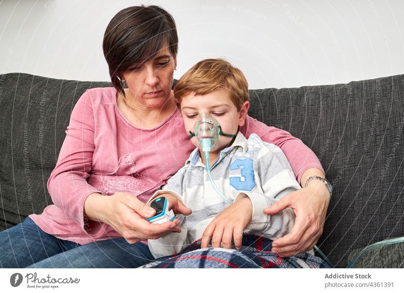 Mother using pulse oximeter on finger of child in oxygen mask mother measure together inhale procedure sick home medical patient health care ill kid help check