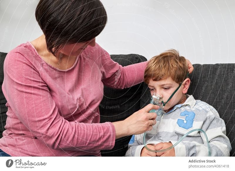 Mother putting on oxygen mask on face of child for inhalation mother put on inhale procedure sick ill breathe together home son parent care kid content help