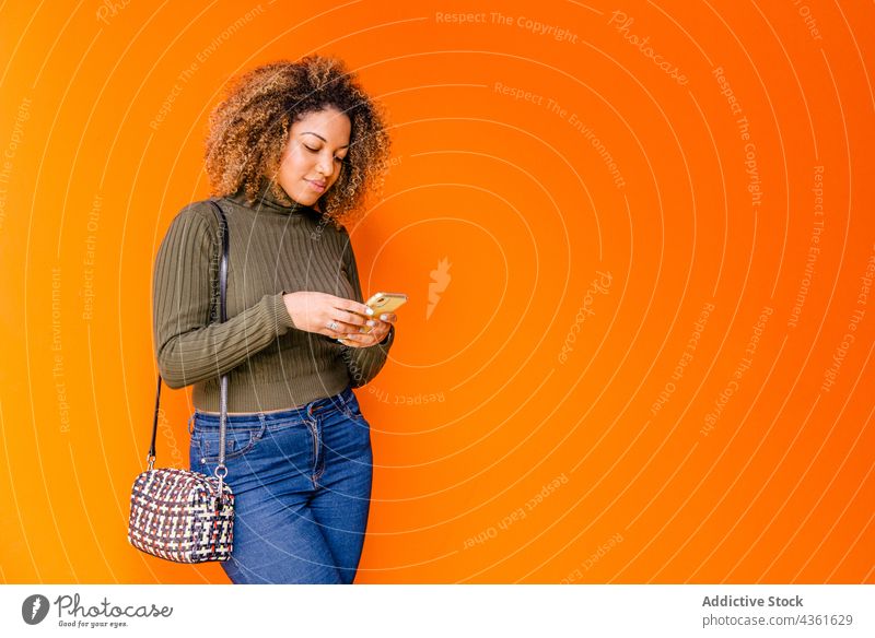 Afro woman using mobile with an orange wall afro person chatting phone technology african background internet smartphone texting female hair isolated digital