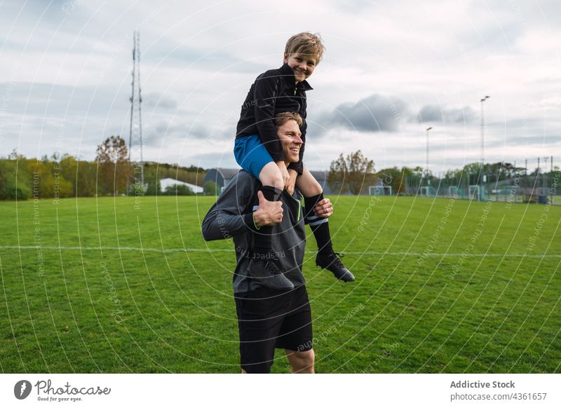 Father and son playing football in field father together carrying shoulder teenage player soccer boy game activity having fun grass parent fatherhood parenthood