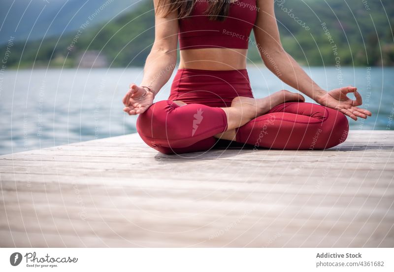 Flexible woman meditating in Lotus pose on pier meditate yoga lotus pose padmasana lake serene practice female gesture water healthy mudra sit vitality