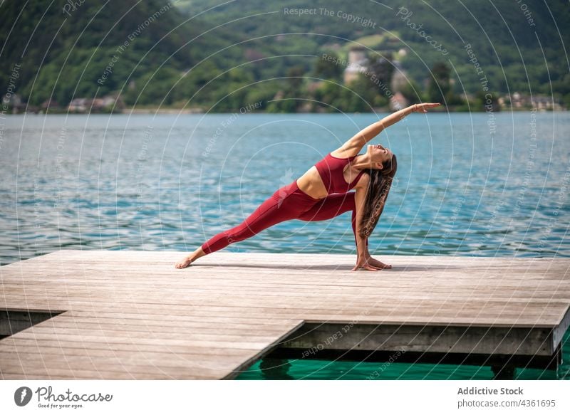 Woman doing yoga in Extended Side Angle pose on pier woman extended side angle pose practice flexible stretch lake utthita parshvakonasana female quay water