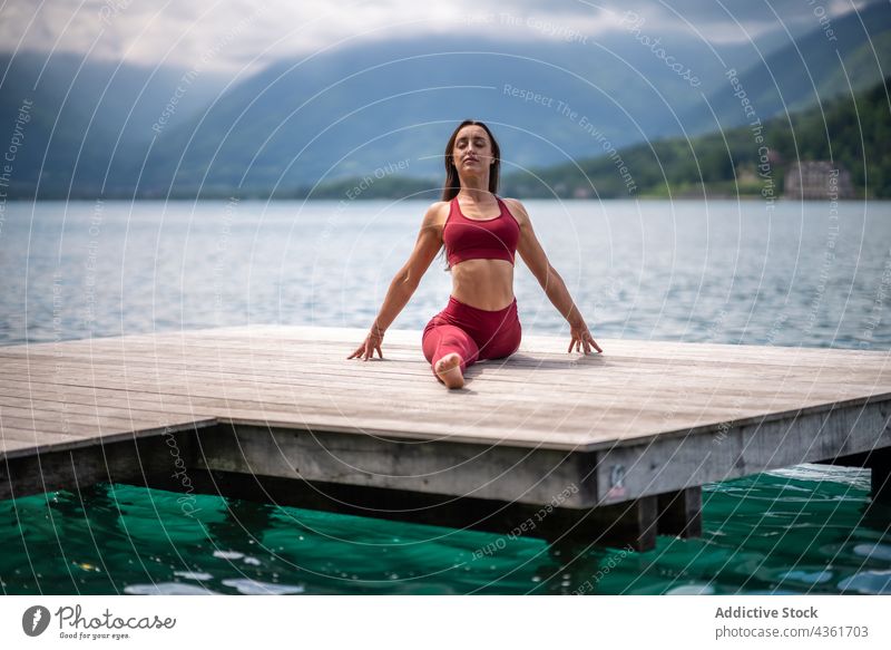 Flexible woman siting in Front Splits pose and doing yoga split stretch flexible pier lake practice tranquil female calm asana hanumanasana harmony water serene