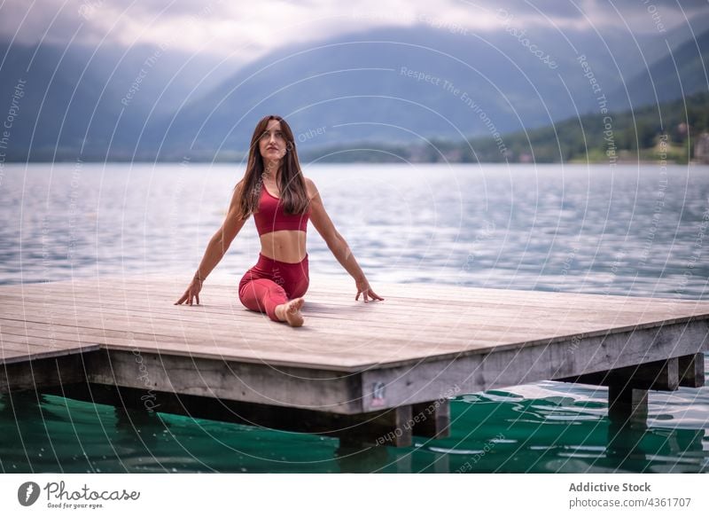 Flexible woman siting in Front Splits pose and doing yoga split stretch flexible pier lake practice tranquil female calm asana hanumanasana harmony water serene