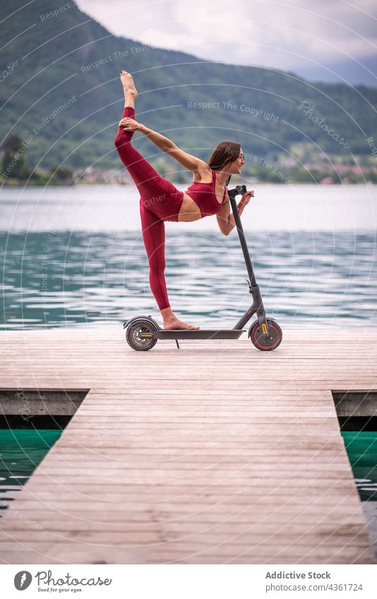 Smiling woman doing yoga in Standing Bow pose on electric scooter standing bow pose practice balance natarajasana flexible female healthy transport vehicle