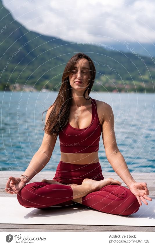 Flexible woman meditating in Lotus pose on pier meditate yoga lotus pose padmasana lake serene practice female water healthy tranquil sit vitality quiet
