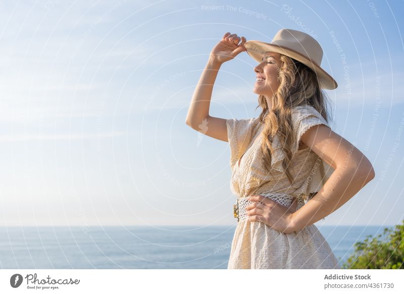 Happy woman in stylish summer outfit standing near sea fashion look dress hat eyes closed style vacation holiday young female happy charming enjoy travel