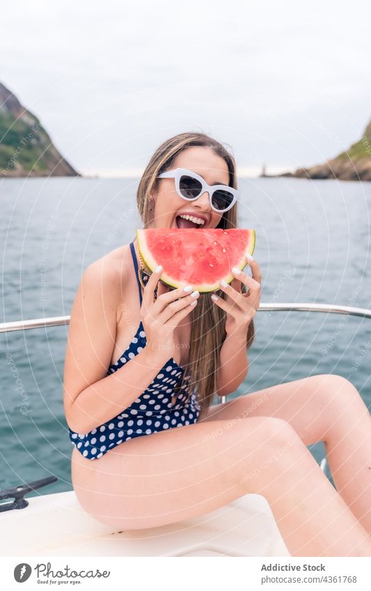 Young girl with glasses and swimsuit on a sailing boat eating a slice of watermelon woman summer person swimwear fun happy ocean yacht sunglasses vacation