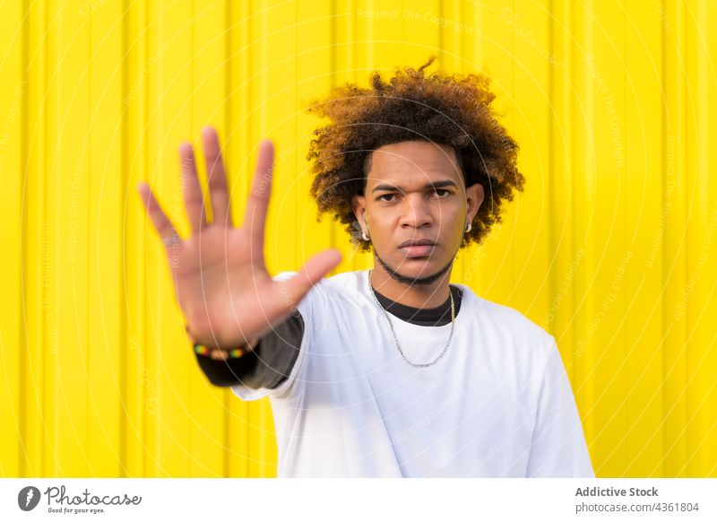 Black man showing stop gesture against yellow wall sign prohibit reject forbidden no refuse serious male ethnic black african american style urban afro city