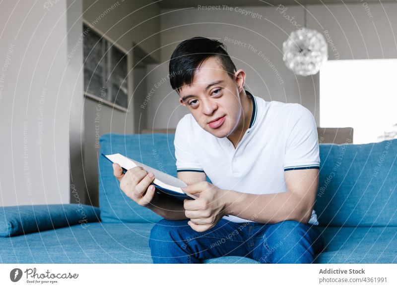 Latin boy with Down syndrome reading book at home down syndrome teen interesting literature sofa hobby ethnic latin teenage couch sit living room knowledge