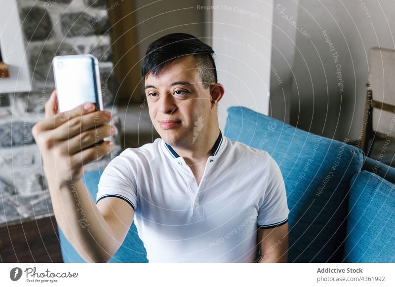 Teen ethnic boy with Down syndrome taking selfie at home down syndrome smile smartphone self portrait disorder memory moment teenage happy latin device sofa