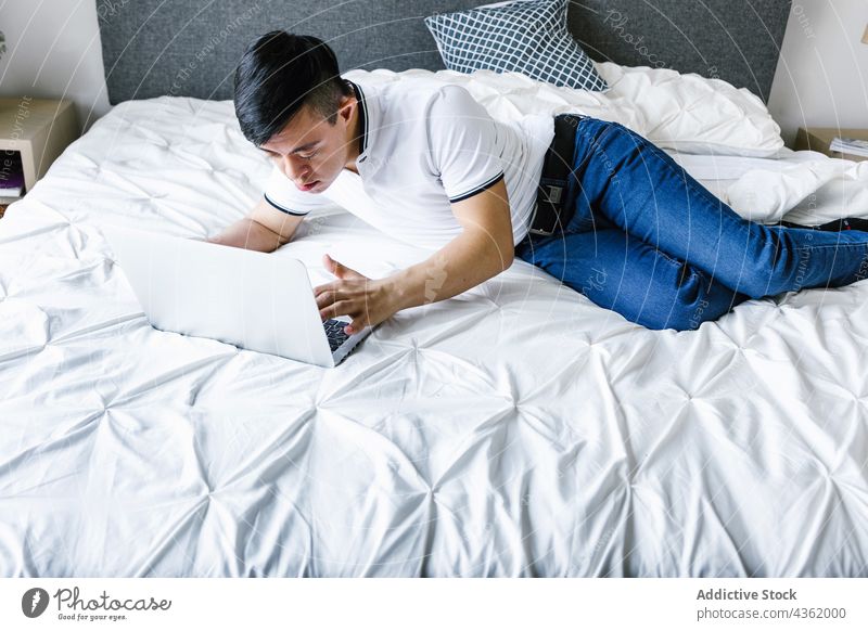 Ethnic teenage boy with Down syndrome browsing laptop at home down syndrome lying bed surfing using ethnic latin entertain gadget internet concentrate device