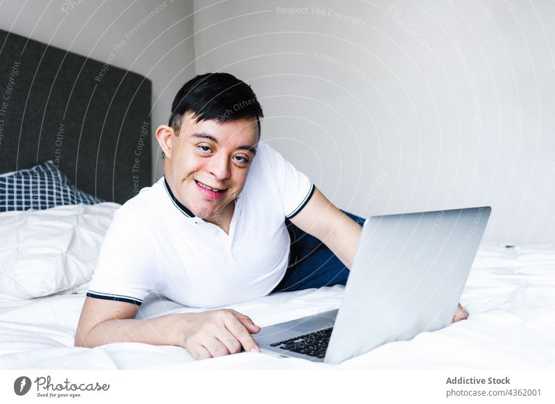 Ethnic teenage boy with Down syndrome browsing laptop at home down syndrome lying bed surfing using ethnic latin entertain gadget internet concentrate device