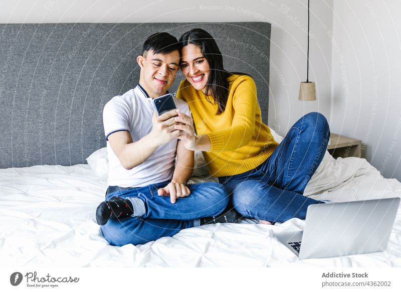 Cheerful Latin mother and son with Down syndrome taking selfie at home down syndrome self portrait smartphone moment together love ethnic latin boy cheerful