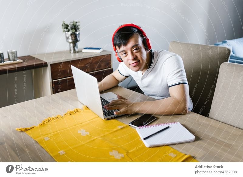 Smiling ethnic teenager with Down syndrome using laptop during remote studies boy study home down syndrome education browsing disorder student latin internet