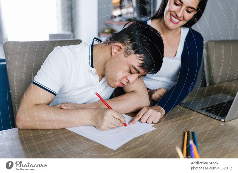 Latin boy with Down syndrome drawing at table with mother down syndrome paper creative son together entertain disorder ethnic latin freelance work laptop mom