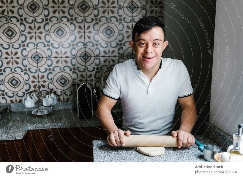 Happy Latin boy with Down syndrome rolling dough at table down syndrome cook cheerful teenage prepare pastry kitchen ethnic latin smile happy home food