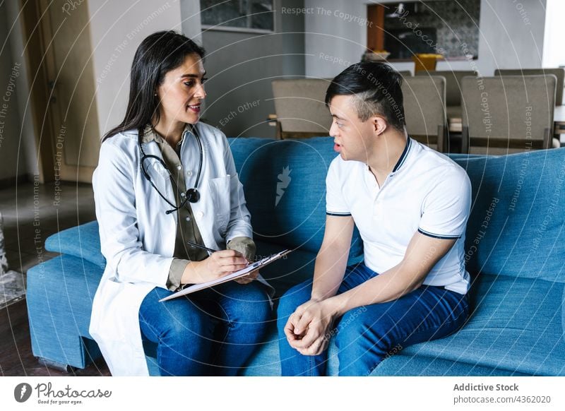 Content doctor talking to Latin boy with Down syndrome during visit at home patient appointment down syndrome take note write ethnic latin speak professional