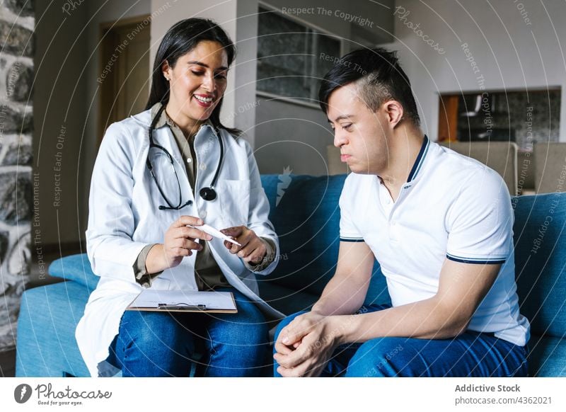 Content doctor talking to Latin boy with Down syndrome during visit at home patient appointment down syndrome take note write ethnic latin speak professional