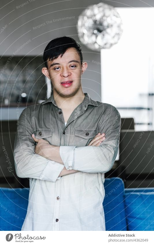 Content ethnic boy with Down syndrome standing in room at home down syndrome smile teenage arms crossed disorder happy cheerful latin casual joy positive calm