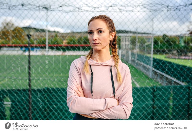 Serious sportswoman with boxer braids posing with crossed arms serious athlete looking aside girl power hard woman sports field metal fence active female hood