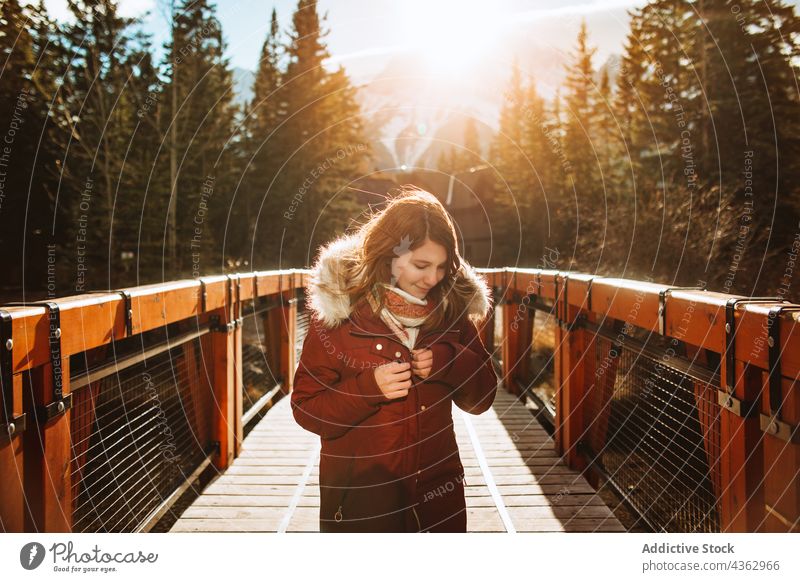 Happy traveling woman standing on footbridge in forested highlands traveler mountain autumn sunlight nature landscape alone journey environment wanderlust