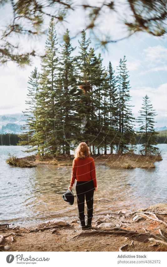 Anonymous person standing looking at islet with coniferous trees in lake woman traveler nature shore water alberta canada banff national park landscape scenic