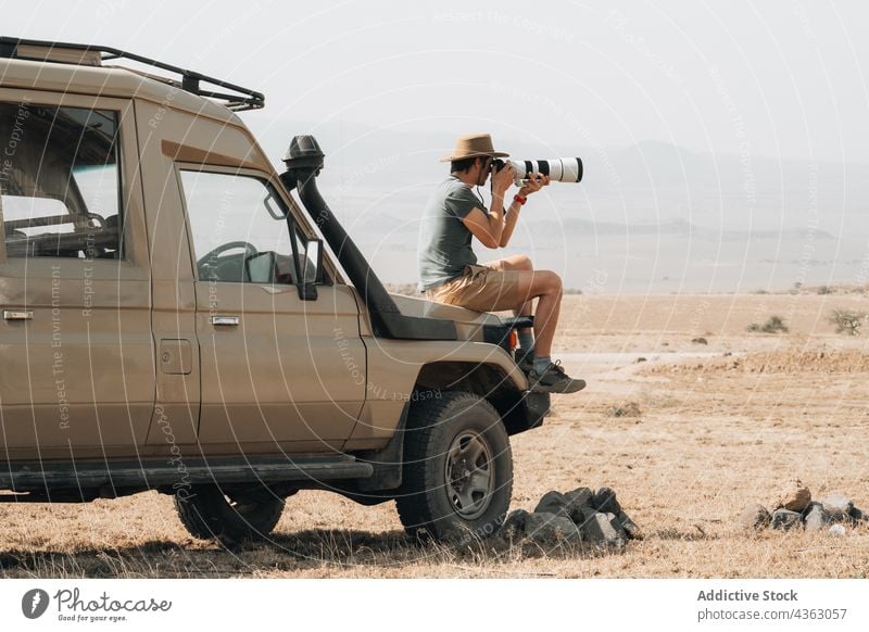 Traveling photographer taking photos during safari travel man take photo photo camera photography telephoto lens traveler male offroad off road car adventure