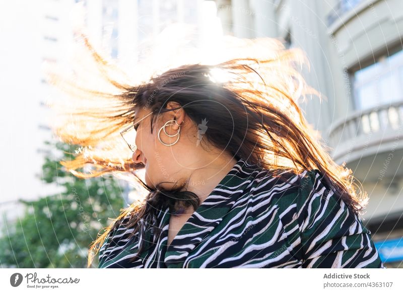 Stylish long haired woman having fun on street style earring sunlight summer urban happy fashion young female accessory flying hair shaking hair cheerful trendy