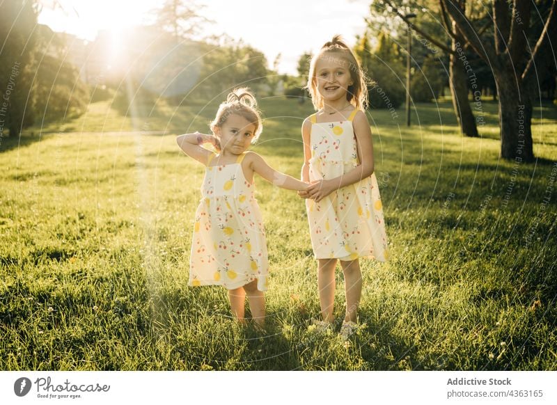 Happy little siblings in similar dresses in summer park girl sister together nature kid happy children sunlight green childhood holding hands love relationship