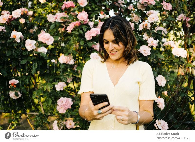 Happy woman using smartphone in blooming garden flower gadget mobile happy female blossom device browsing young smile communicate spring message bush internet