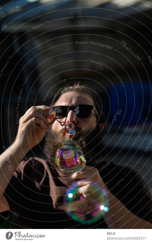 Young man in the shade, blowing colorful bubbles in the sun. Sunlight Sunglasses Facial hair bearded Man Masculine portrait Human being Youth (Young adults)